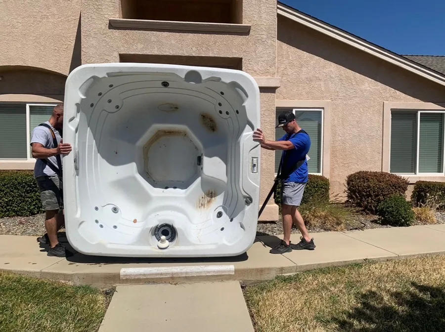 Movers handling a large hot tub outside a home